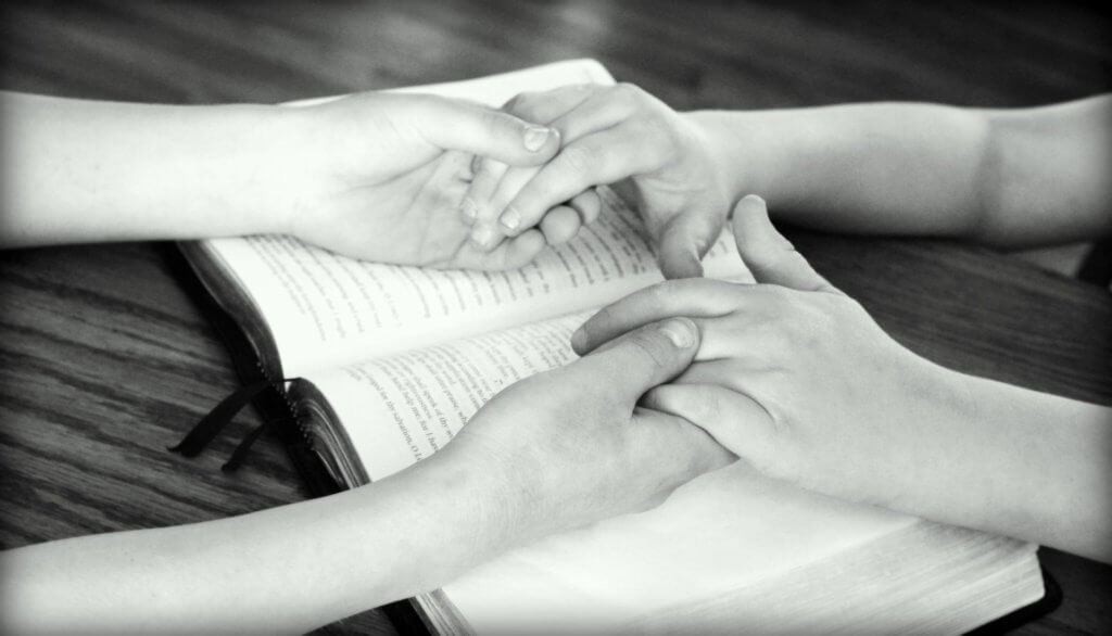 Mother and child holding hands over bible showing the importance of praying with your children.